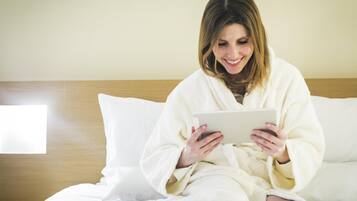 Una persona sentada en una cama, vestida con una bata blanca y sosteniendo una tableta.