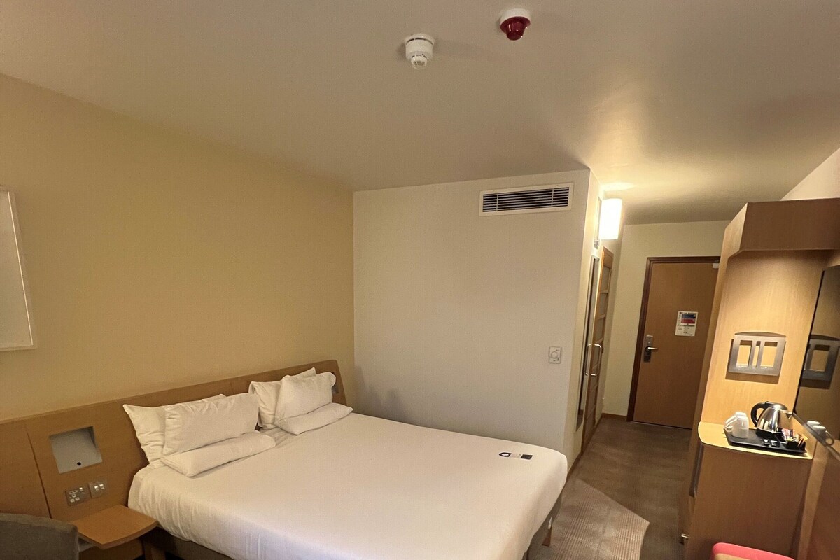 A hotel room with a large bed, a small table, a desk, and a kitchenette.