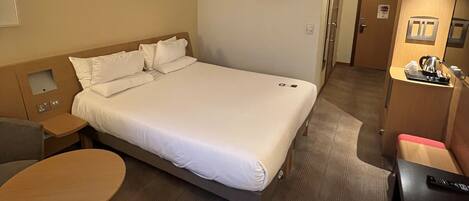 A hotel room with a large bed, a small table, a desk, and a kitchenette.