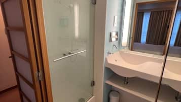 Un baño moderno con ducha envuelta en vidrio, un lavabo blanco y un espejo que refleja la habitación.