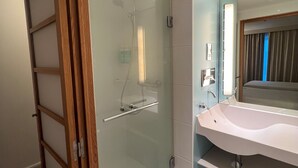 A modern bathroom with a glass-enclosed shower, a white sink, and a mirror above it.