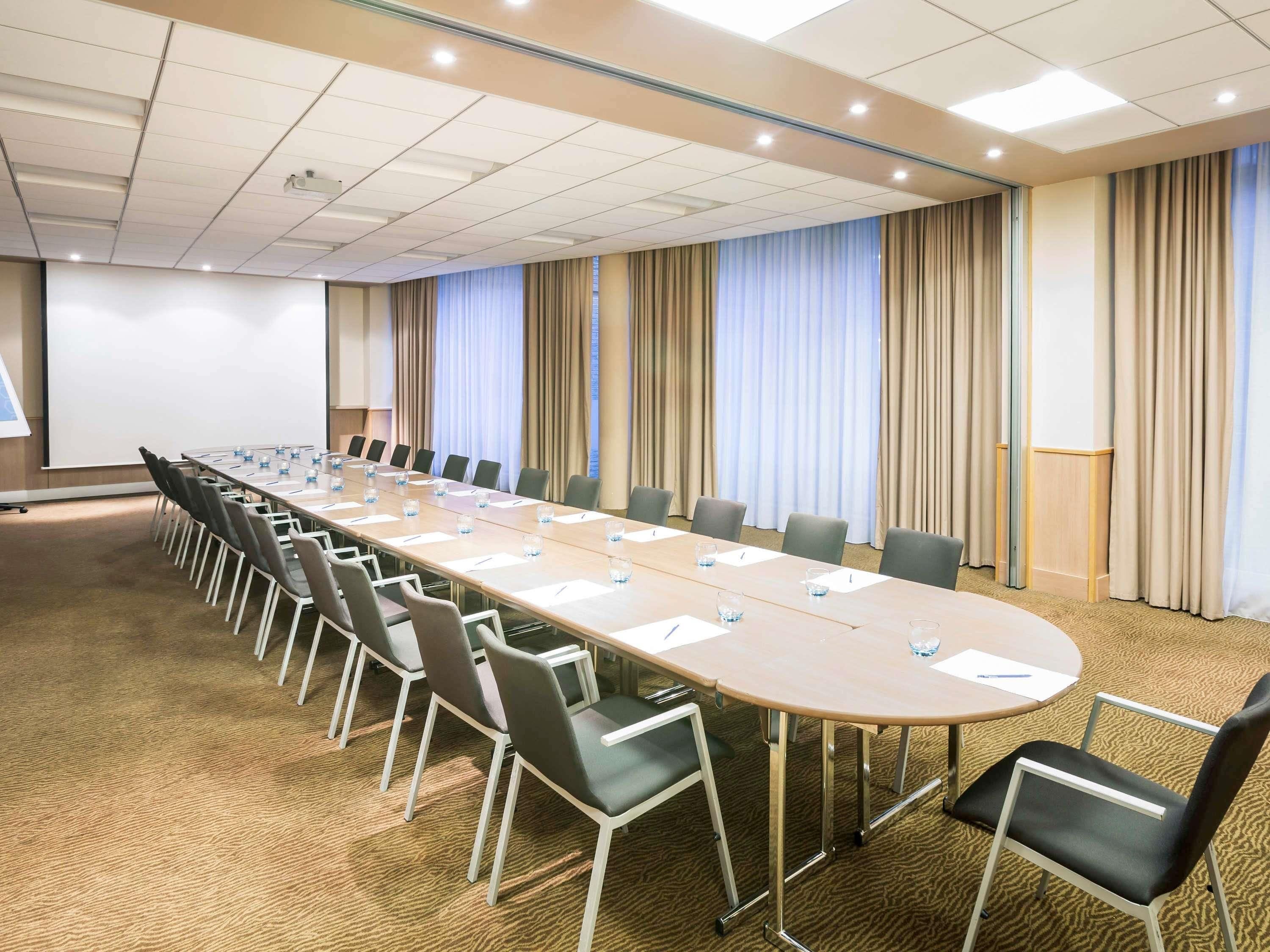 A conference room with a long table, chairs, a projector screen, and curtains.