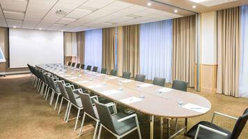 A conference room with a long table, chairs, a projector screen, and curtains.