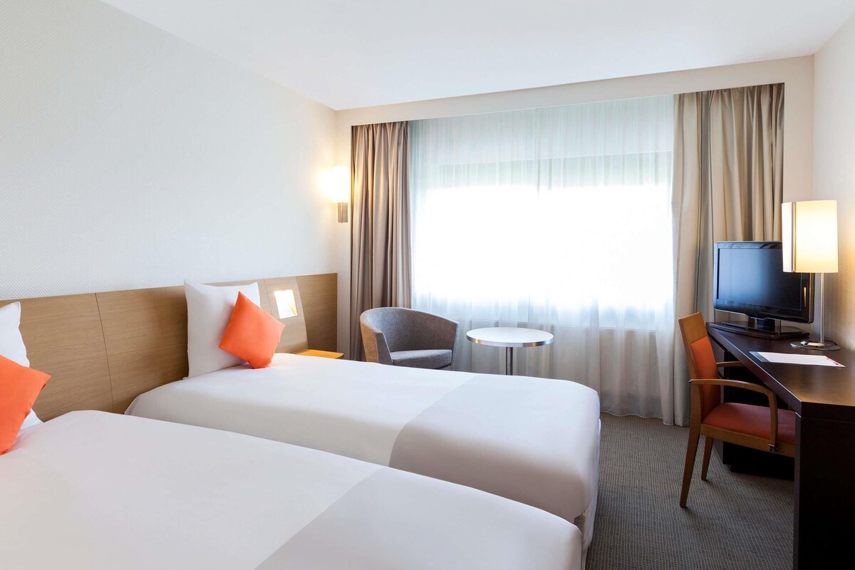 A hotel room with two beds, a desk with a television, a chair, and a small table.
