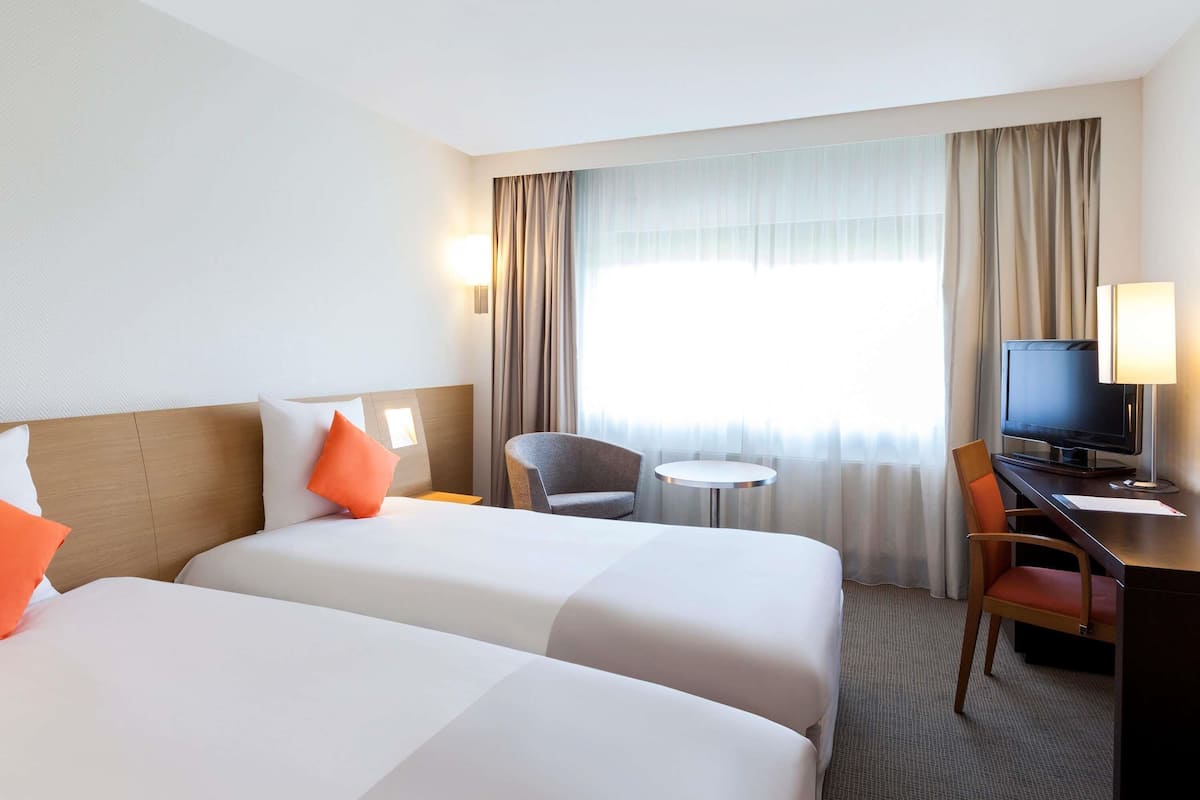 A hotel room with two beds, a desk with a TV, a chair, and a small table.