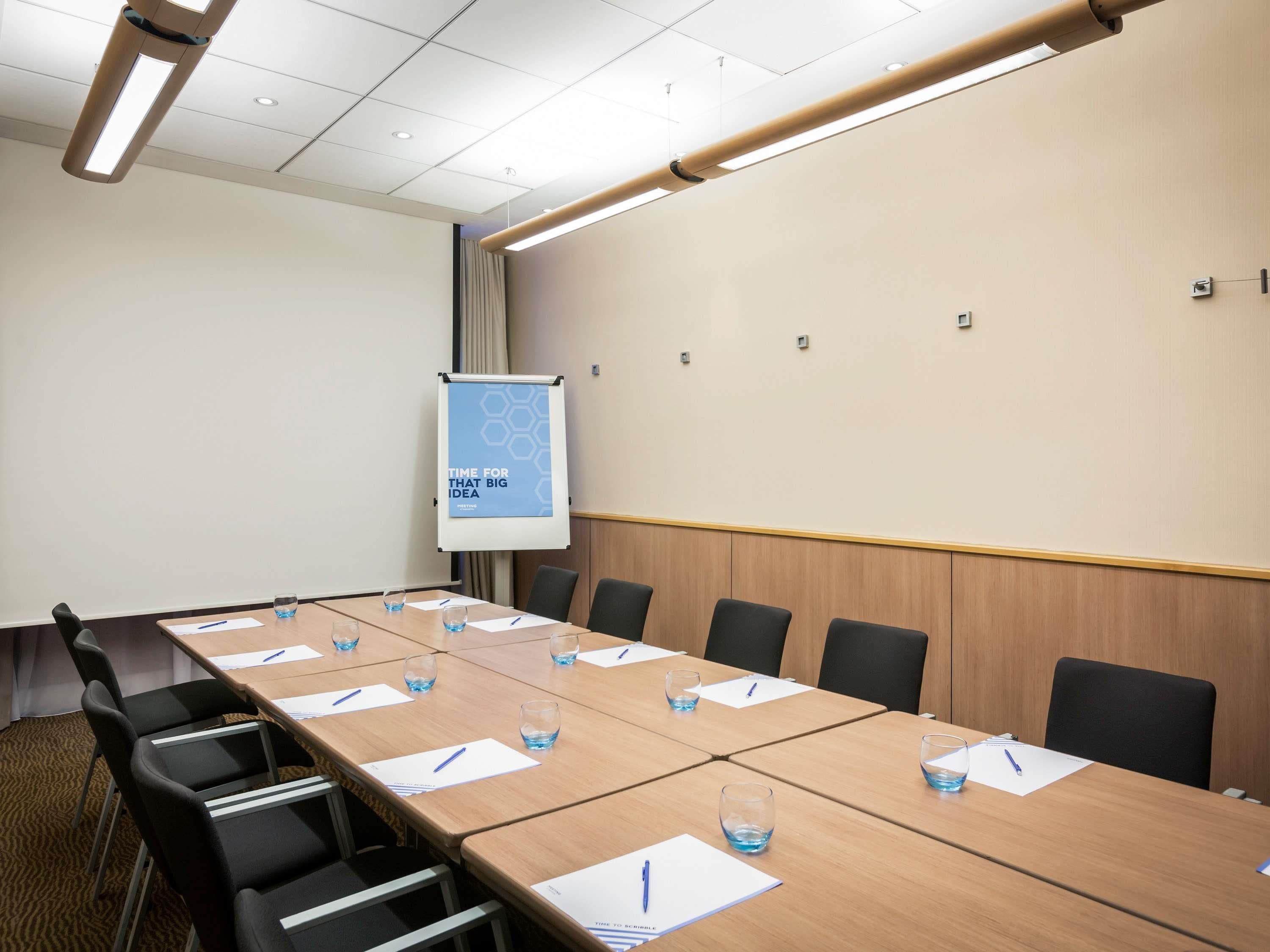A conference room with a long table, chairs, a projector screen, and a presentation on the wall.