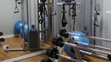 Une salle de sport équipée de divers appareils d’entraînement, notamment une machine à câbles, des piles de poids et des ballons d’exercice.