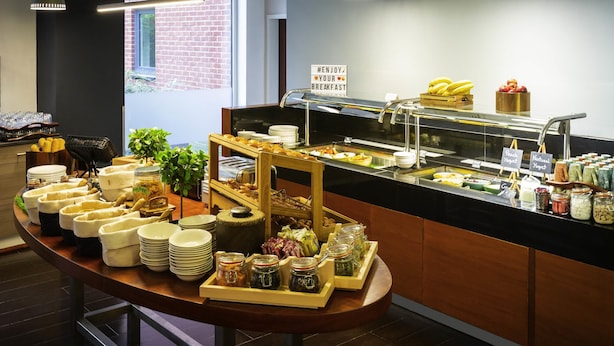Un bufé de desayuno con diversas opciones de comida, un cartel que dice 'Enjoy Your Breakfast' y una pared de ladrillo al fondo.
