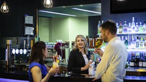 Zona de bar con mostrador, distintas botellas y lámparas colgantes.