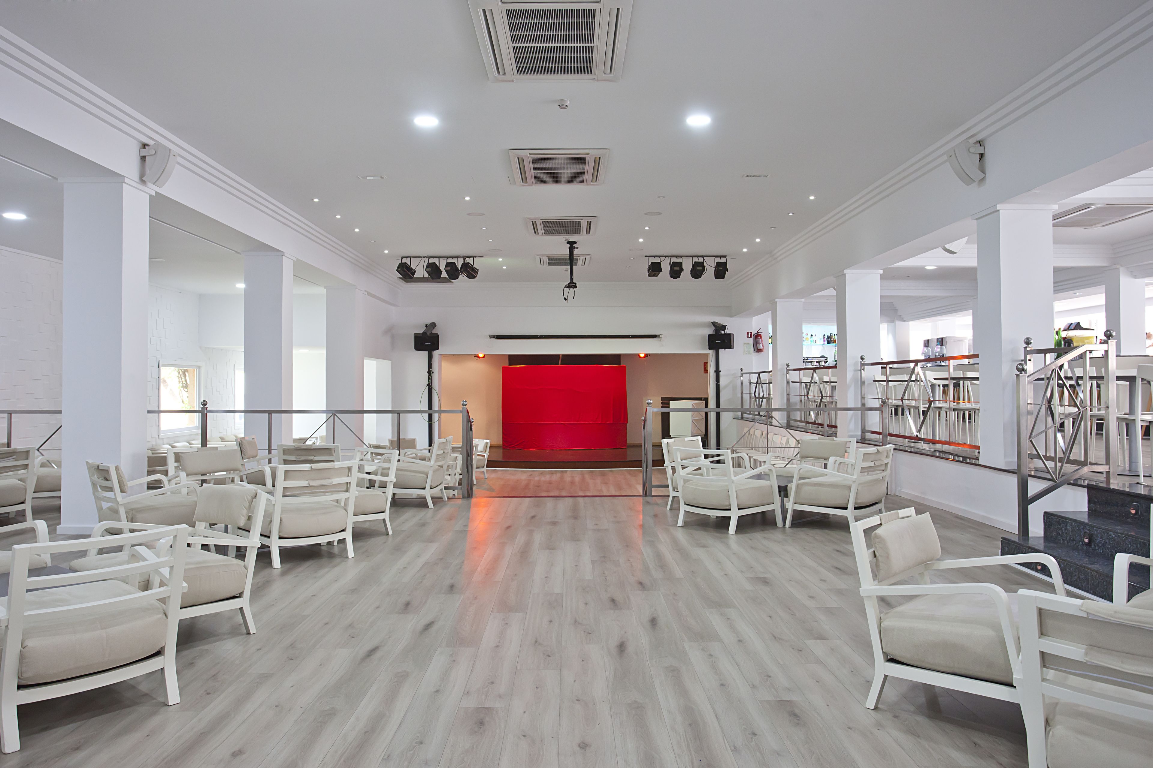 Una habitación amplia con filas de sillas blancas, un telón de fondo rojo y un escenario.