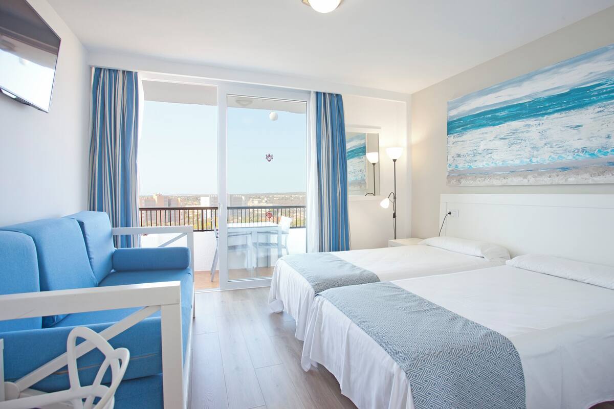 Habitación de hotel con dos camas, un balcón con vistas, un sofá y un televisor.