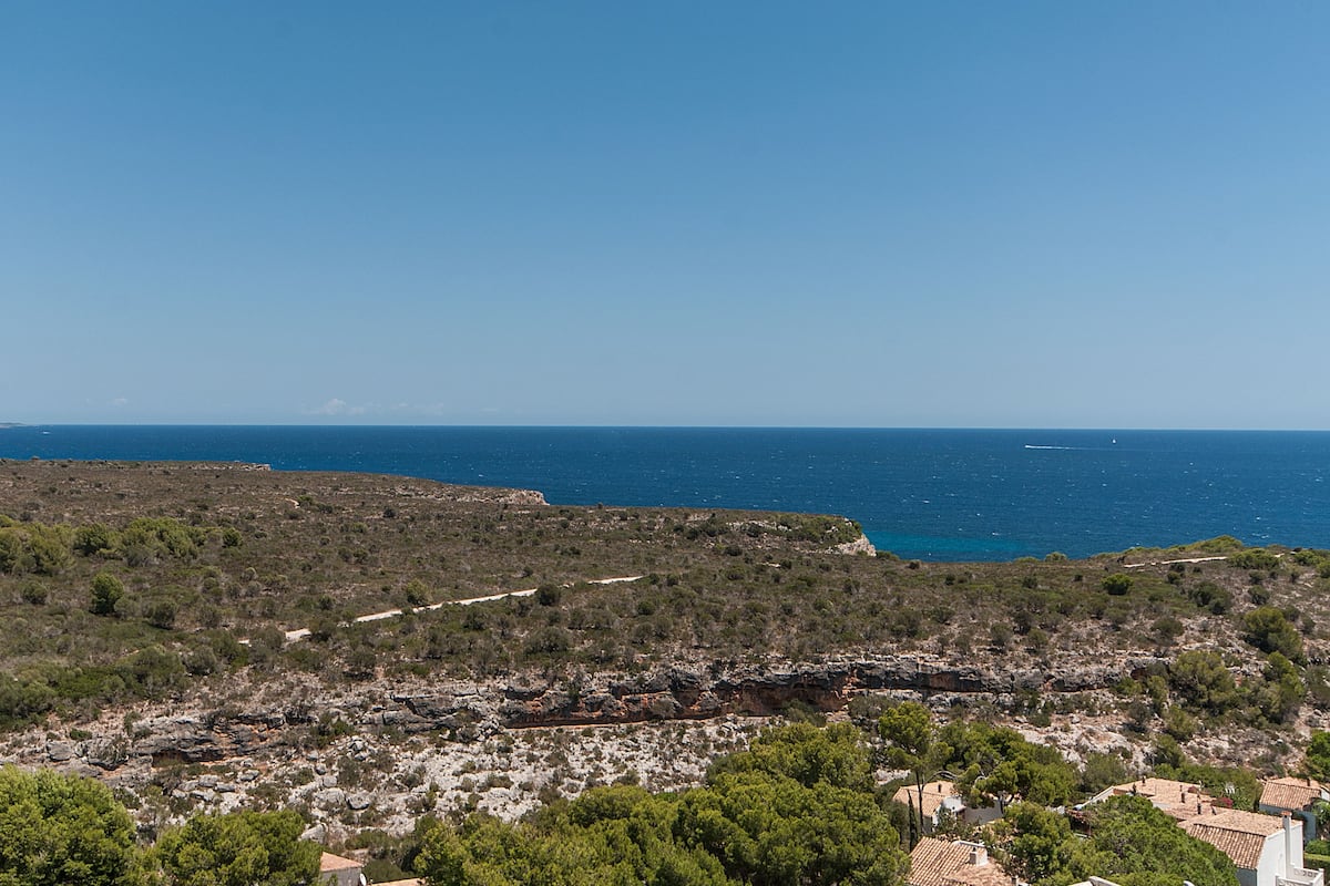 Un paisaje costero con terreno rocoso y vegetación escasa, con vista a un mar azul y despejado.