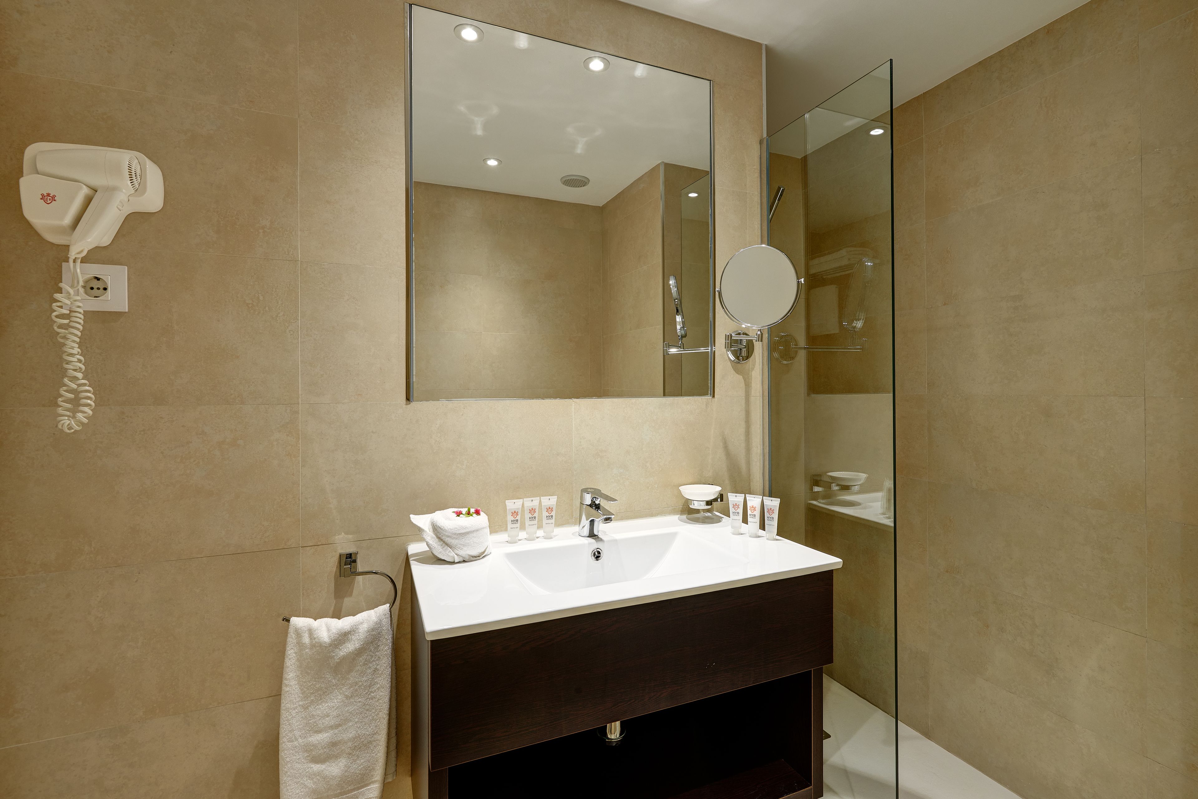A modern bathroom with a large mirror, a white sink, and a hairdryer on the wall.