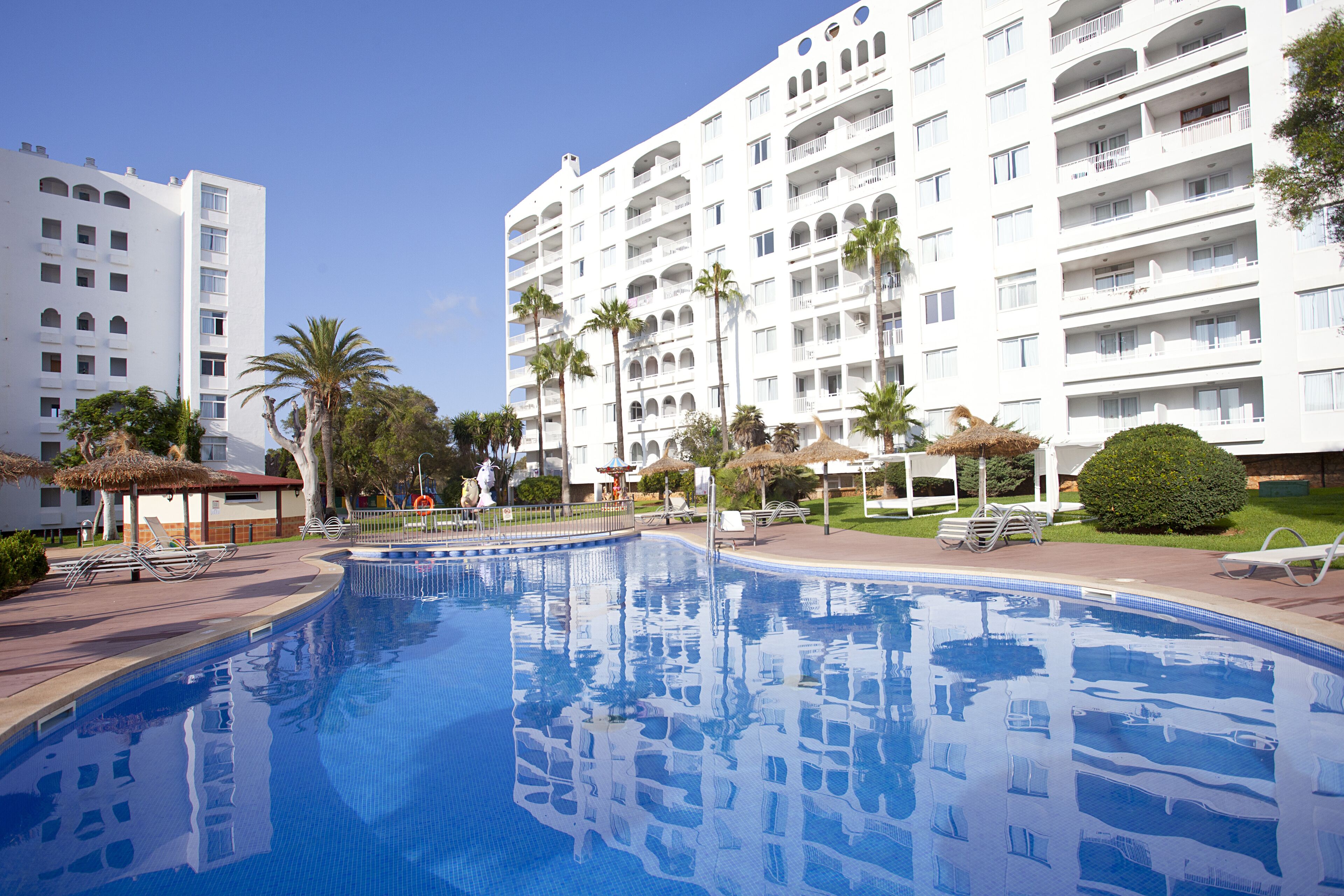 Un hotel con piscina circondata da palme e sdraio.