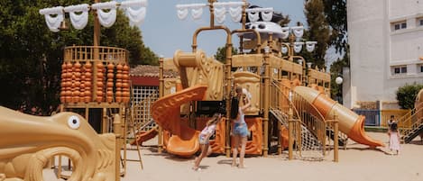 Een kinderspeelplaats met een glijbaan, klimconstructies en een grote decoratieve vissenfiguur.