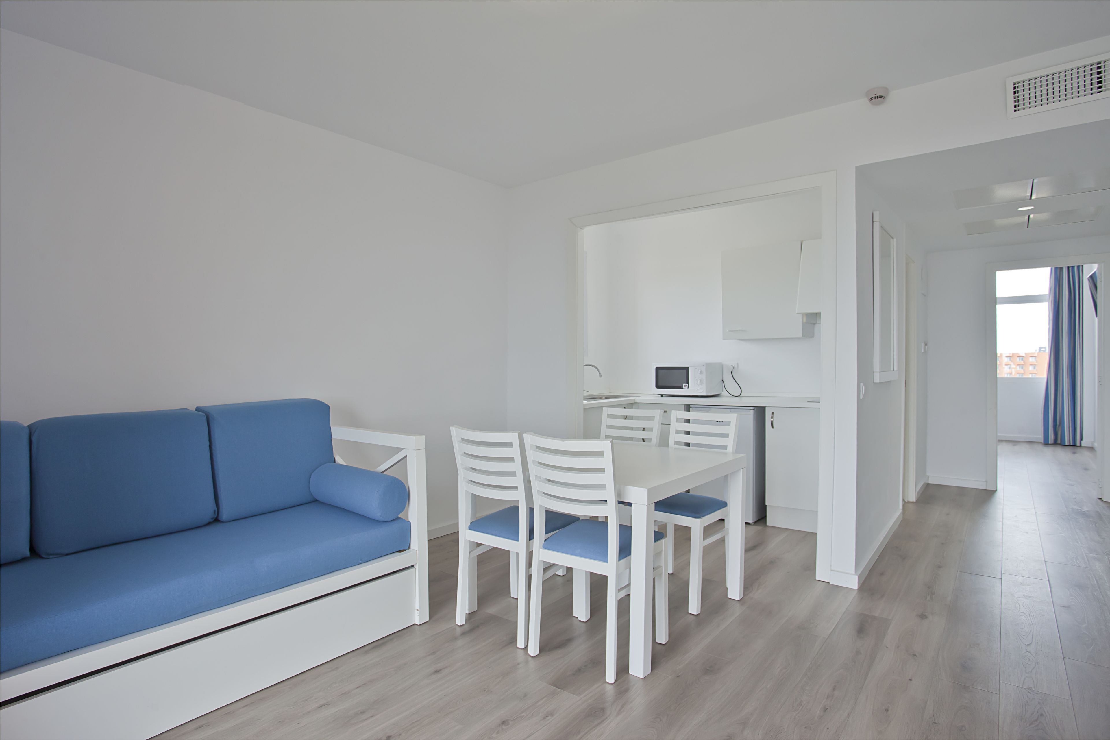 Una sala de estar moderna con un sofá azul, sillas blancas, una mesa de comedor y una zona de cocina con un microondas.