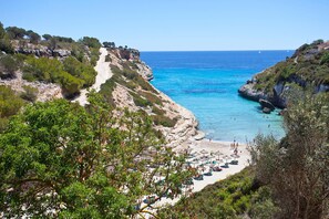Une zone côtière comprenant une plage, des falaises rocheuses et une mer bleue et limpide.