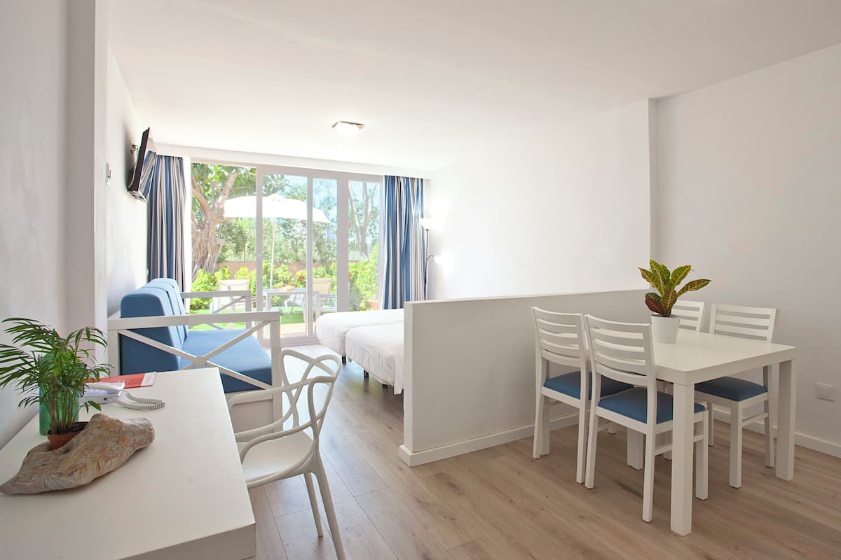 Una habitación moderna con cama, una mesa de comedor con sillas, una planta en maceta y vistas al exterior.