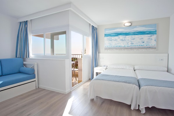 A bedroom with a bed, a sofa, and a balcony with curtains.