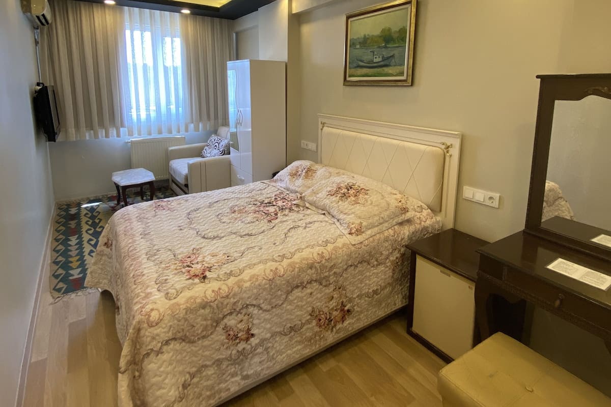 A hotel room with a bed, a desk, a chair, a small table, and a mirror.