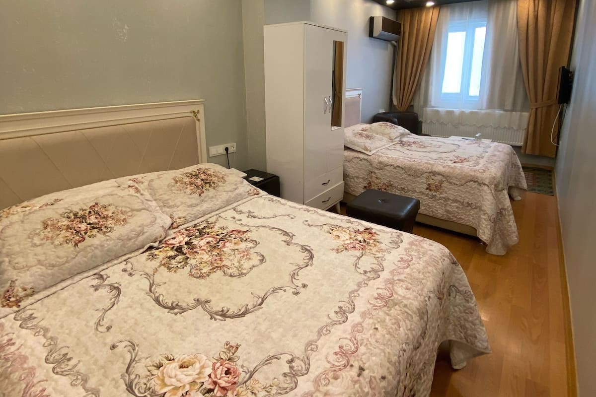 A hotel room with two beds, a wardrobe, a desk, and a window with curtains.