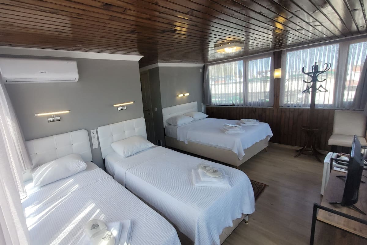 A hotel room with two beds, a wooden ceiling, and a large window with curtains.