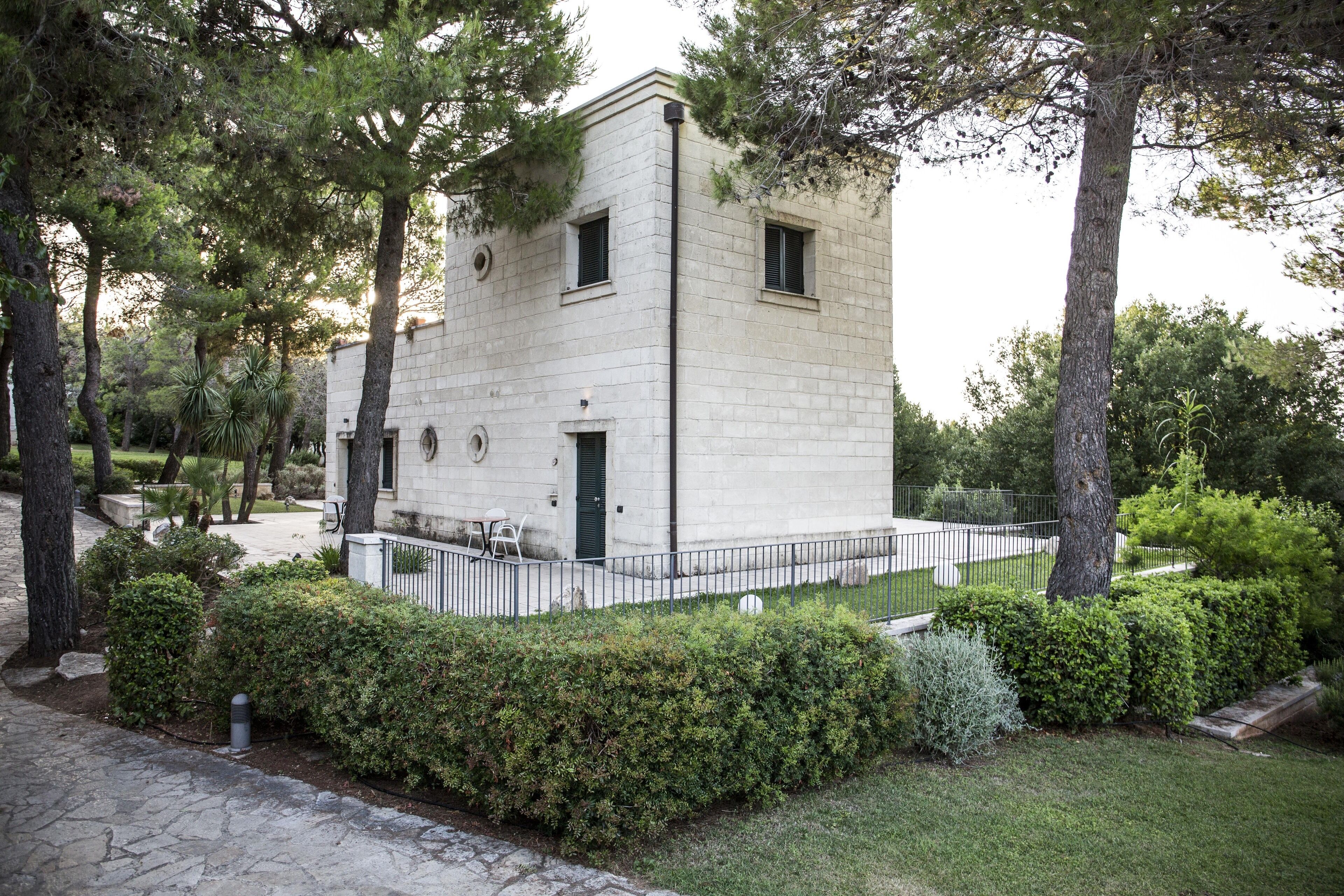 Un edificio moderno con fachada de piedra, rodeado de setos y árboles bien cuidados.