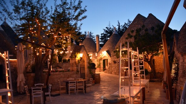 Un patio con edificios de piedra, asientos al aire libre y luces colgantes.