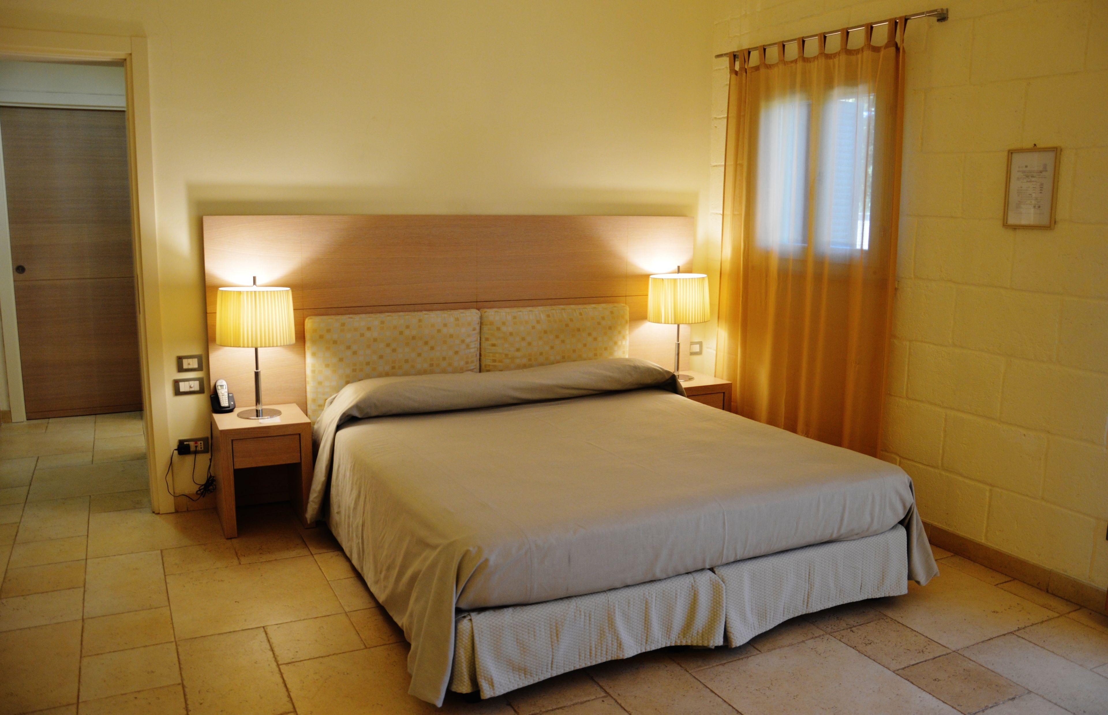 Habitación de hotel con una cama grande, dos lámparas de noche, un cabecero de madera y una cortina en la ventana.