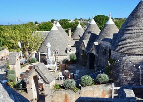 Un cortile con edifici in pietra caratterizzati da tetti a cono, immerso nel verde e con zone salotto all'aperto.