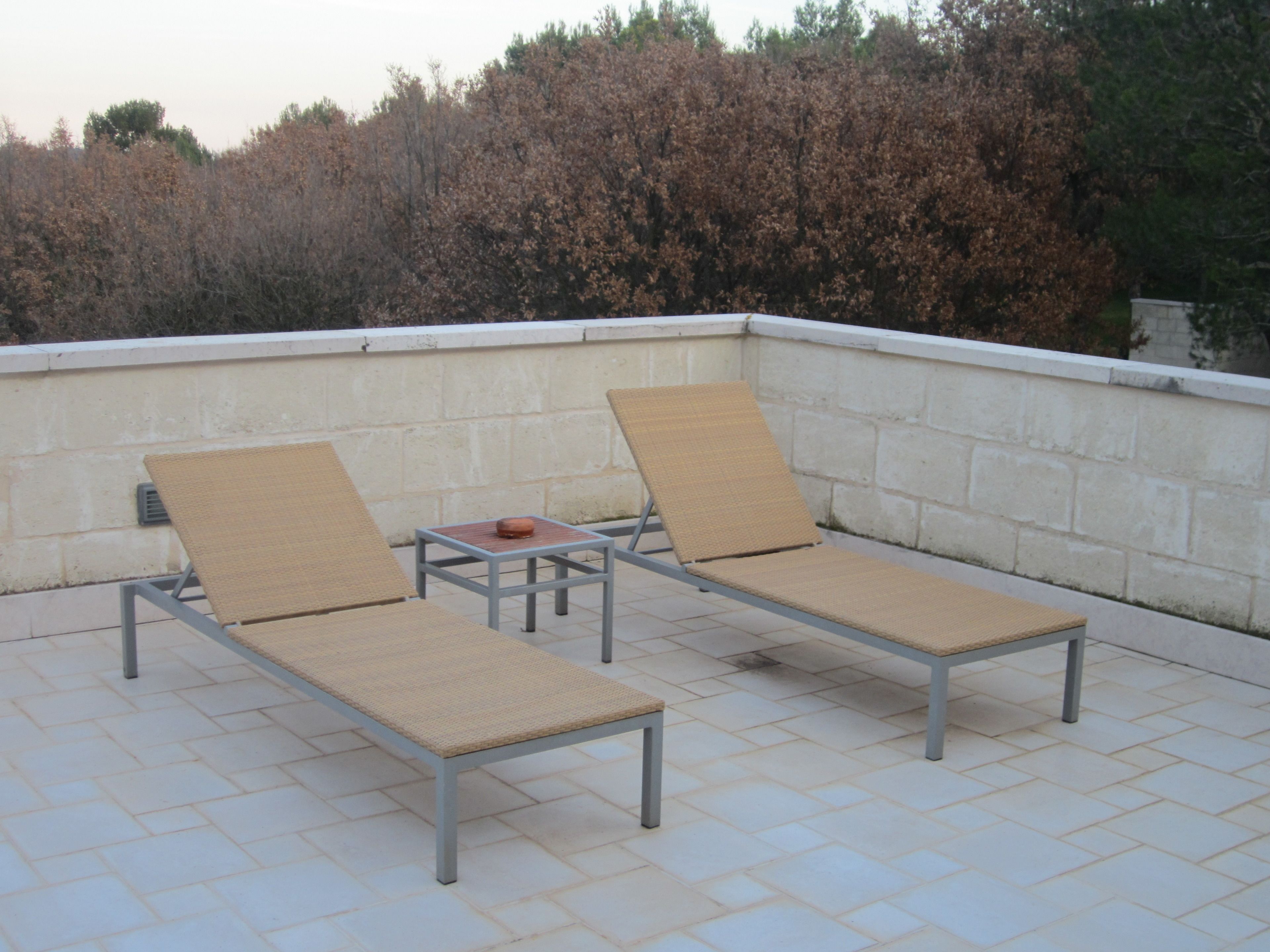 Dos sillones de relax con estructura metálica y asientos tejidos en un patio con baldosas.