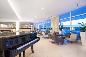 Un moderno vestíbulo de hotel con un piano de cola, zona de estar y amplios ventanales que ofrecen vistas de la ciudad.