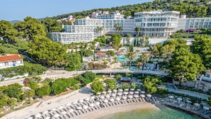 Oversigtsbillede af et kystresort med en klar strand, flere swimmingpools og frodigt grønt område.