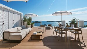 A deck with a sofa, chairs, a table, and umbrellas, overlooking a body of water.