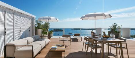 A deck with a sofa, chairs, a table, and umbrellas, overlooking a body of water.