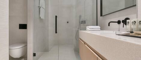 Un baño moderno con cabina de ducha de vidrio, tocador con encimera y un inodoro.