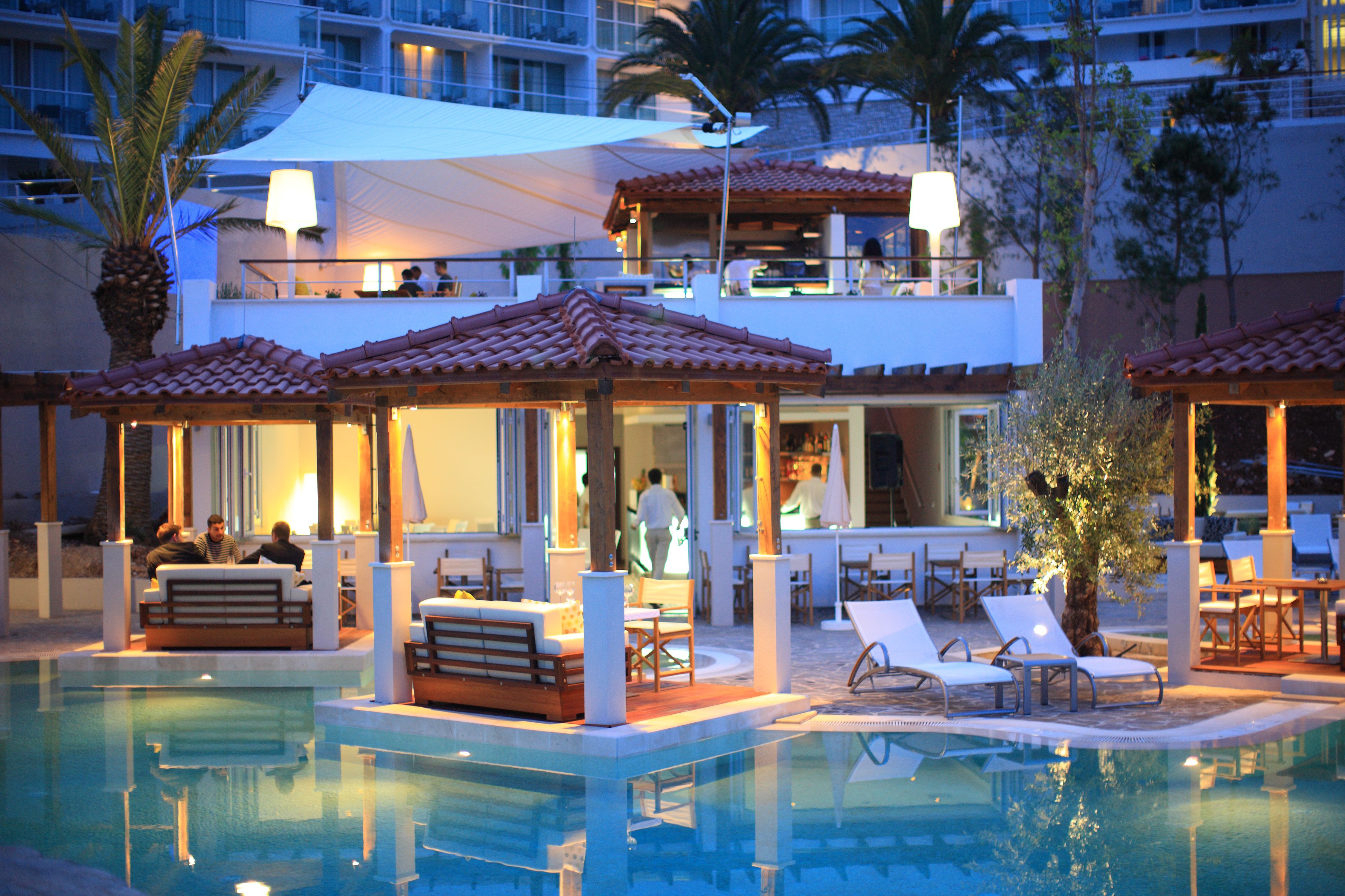 A pool area with lounge chairs and a bar area with tables and chairs.