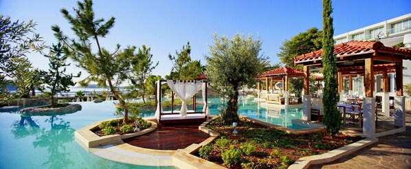 A resort pool area with a gazebo, lounge chairs, and a dining area.