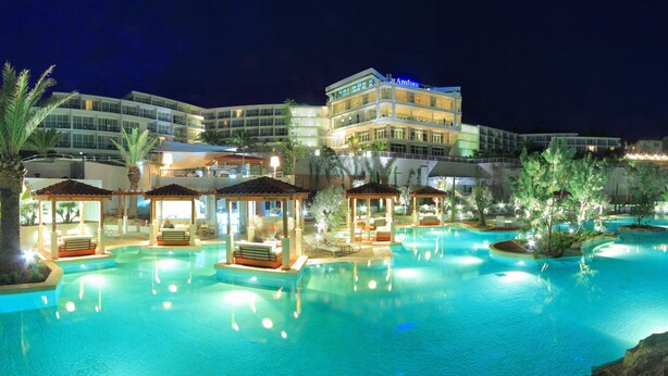 Et hotel med en stor swimmingpool, flere loungeområder og en velbelyst bygning.