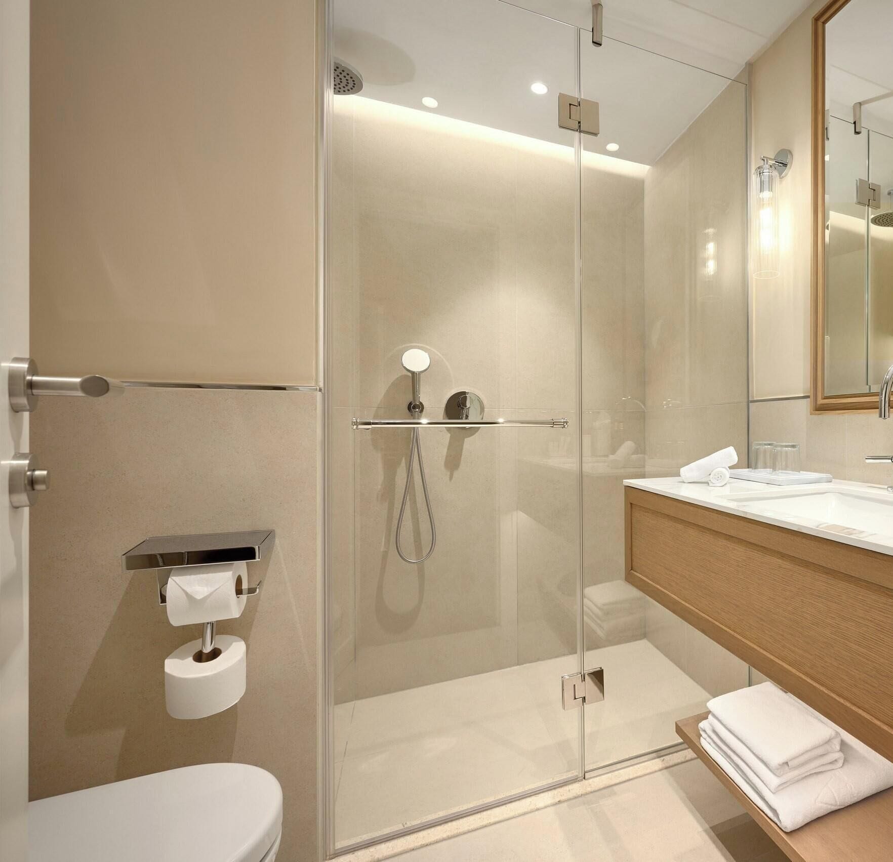 A modern bathroom with a glass-enclosed shower, a toilet, a sink with a mirror, and a towel rack.