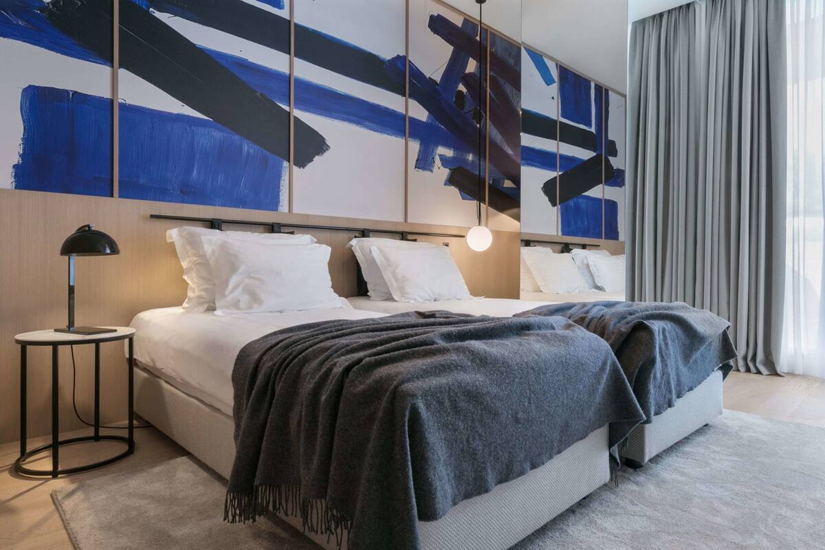 Ein modernes Hotelzimmer mit einem großen Bett, einem Nachttisch und einer Wand mit abstrakter Kunst.