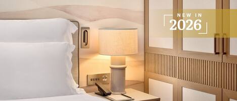 Una habitación de hotel con una cama, una mesita de noche con lámpara, un teléfono y un bloc de notas.