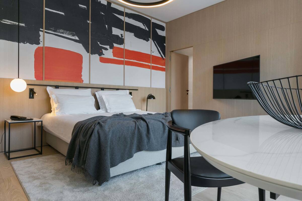 Ein modernes Hotelzimmer mit Bett, Nachttisch und rundem Esstisch mit Stühlen.