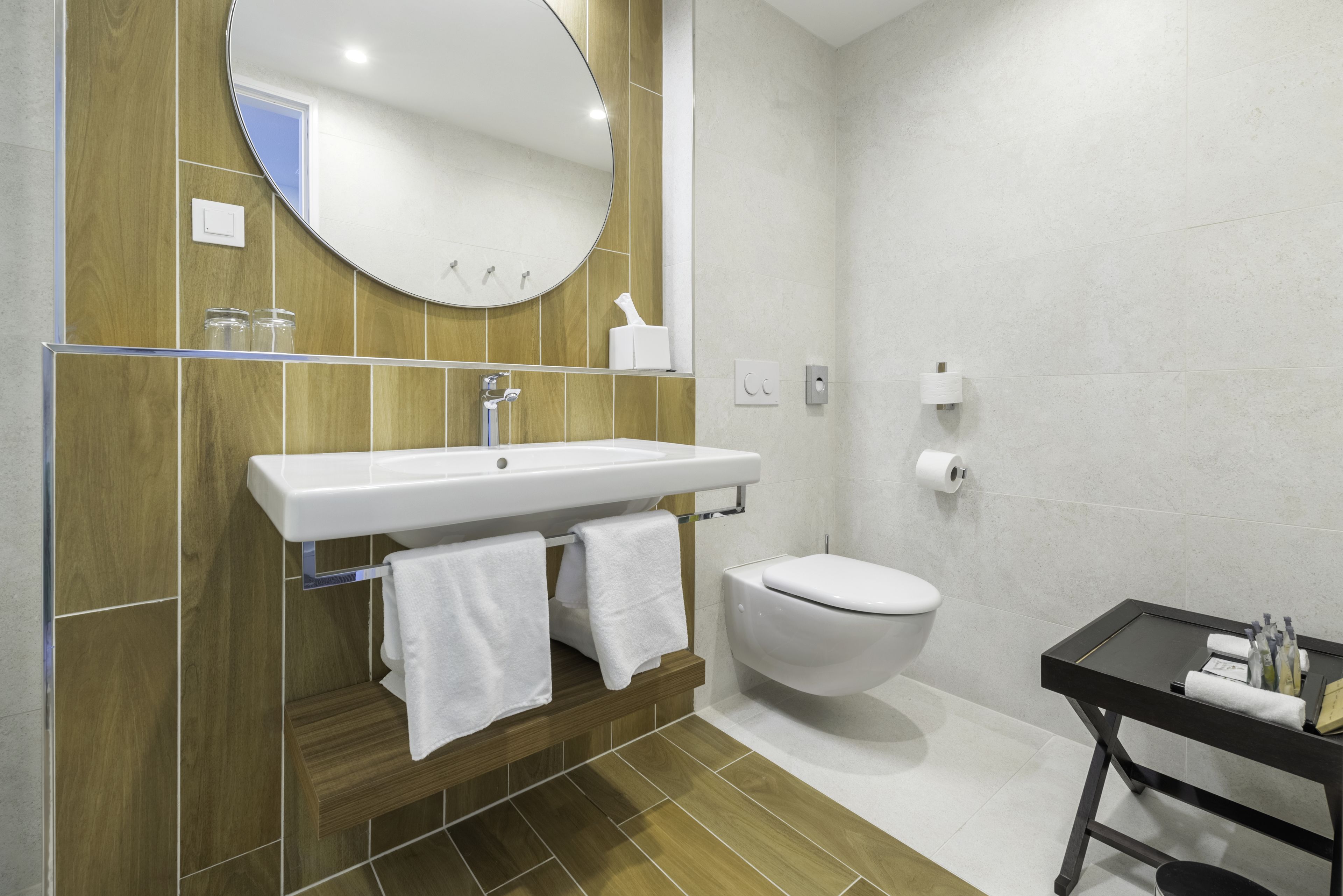 Een moderne badkamer met een houten wastafelmeubel, een witte wastafel en een zwart nachtkastje met toiletartikelen.