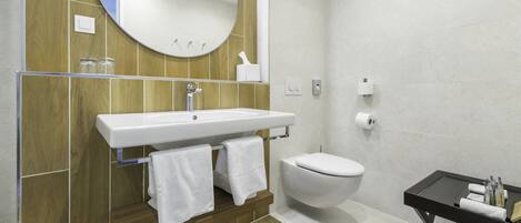 Een moderne badkamer met een houten wastafelmeubel, een witte wastafel en een zwart nachtkastje met toiletartikelen.