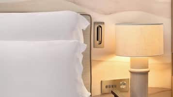 Ein ordentlich bezogenes Bett mit weißen Leinentüchern, ein Nachttisch mit Lampe, Telefon und Steckdose.