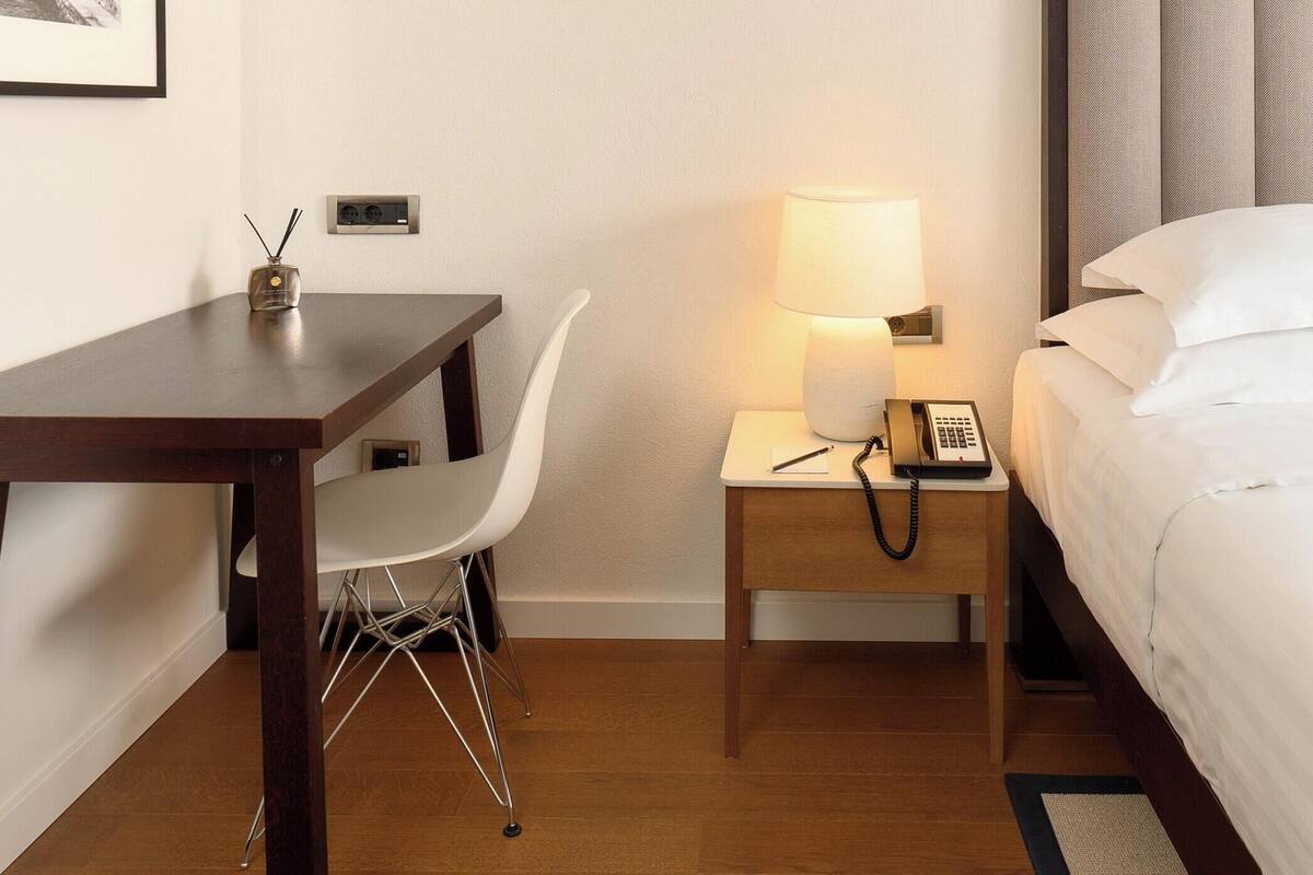 Ein Hotelzimmer mit einem Bett, einem Schreibtisch, einem Stuhl, einer Lampe und einem Telefon.