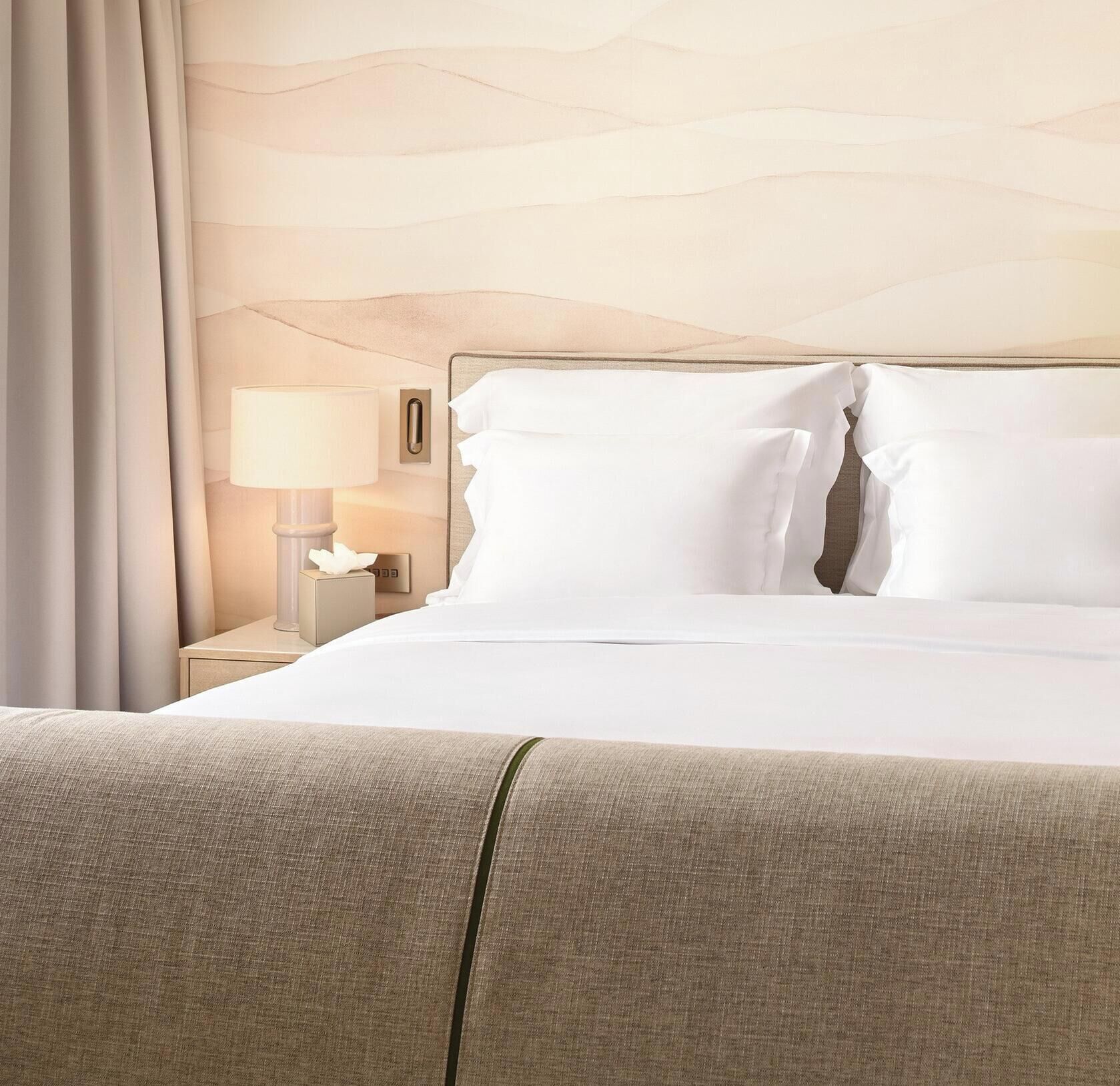 A hotel room with a bed, a nightstand, a lamp, and a wall-mounted light switch.