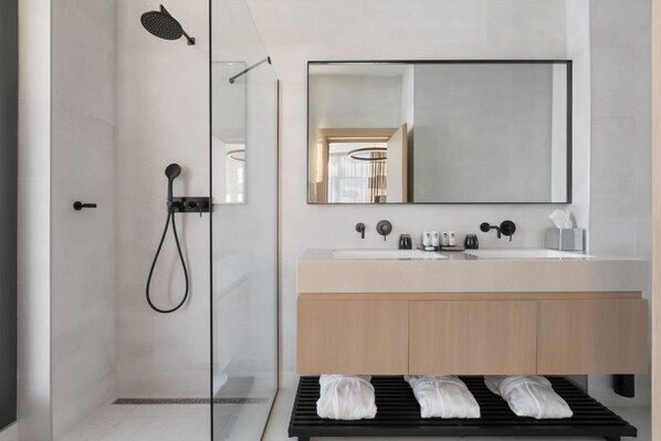 Un baño moderno con ducha envuelta en vidrio, un espejo grande y un tocador de madera.