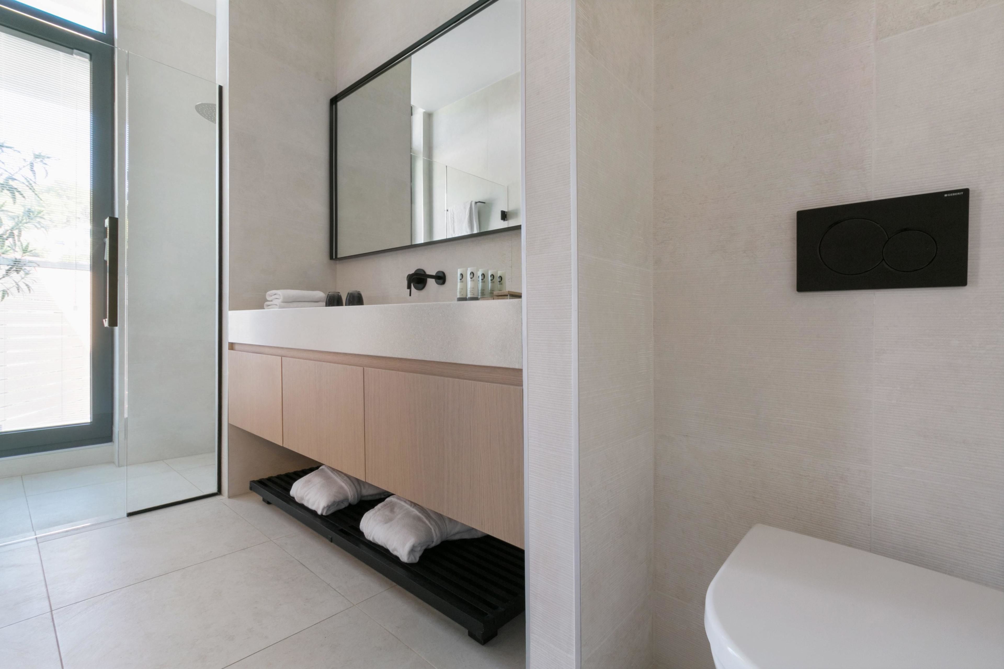 Un baño moderno con puerta de ducha de vidrio, inodoro blanco, tocador de madera y un espejo grande.
